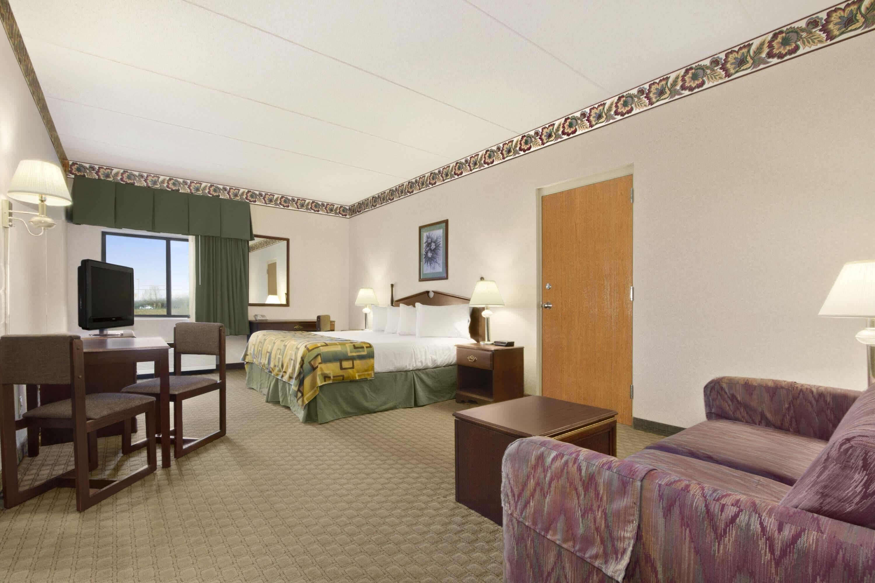 A hotel room with a bed, a desk, a chair, a sofa, and a television.
