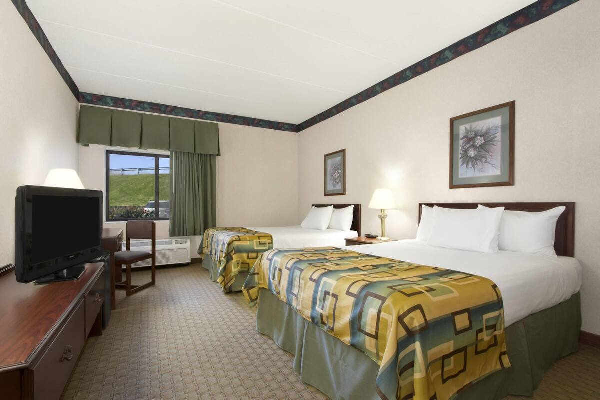 A hotel room with two beds, a television, a desk, and a chair.