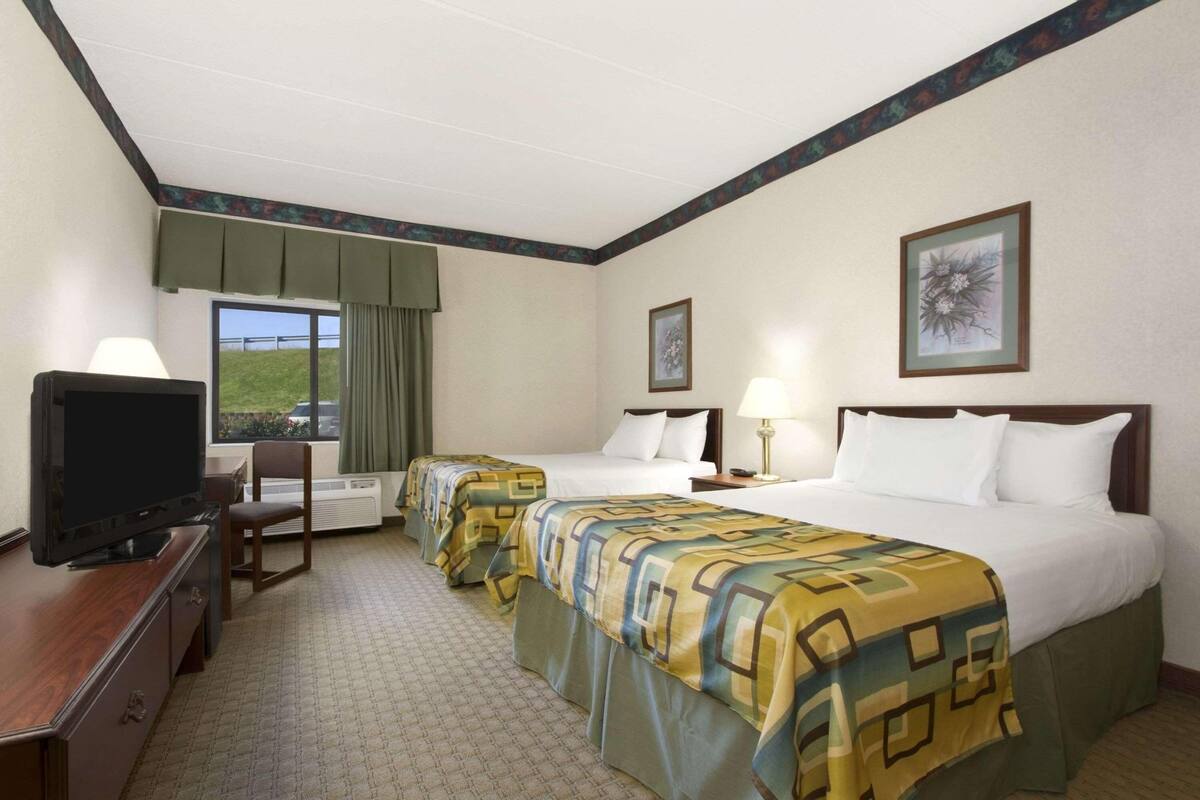 A hotel room with two beds, a TV, a desk, and a window with a view.