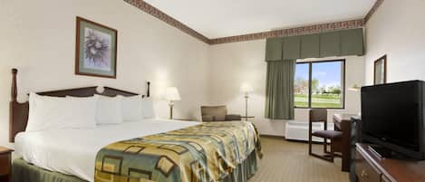 A hotel room with a large bed, a desk with a television, a chair, and a window with a view of greenery.