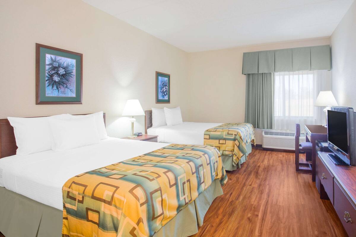 A hotel room with two beds, a TV, and a window with curtains.