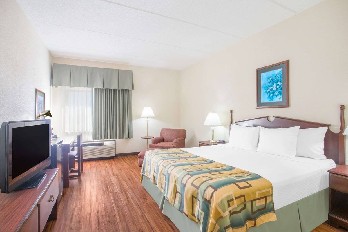 A hotel room with a bed, a TV, a chair, a desk, and a window with curtains.