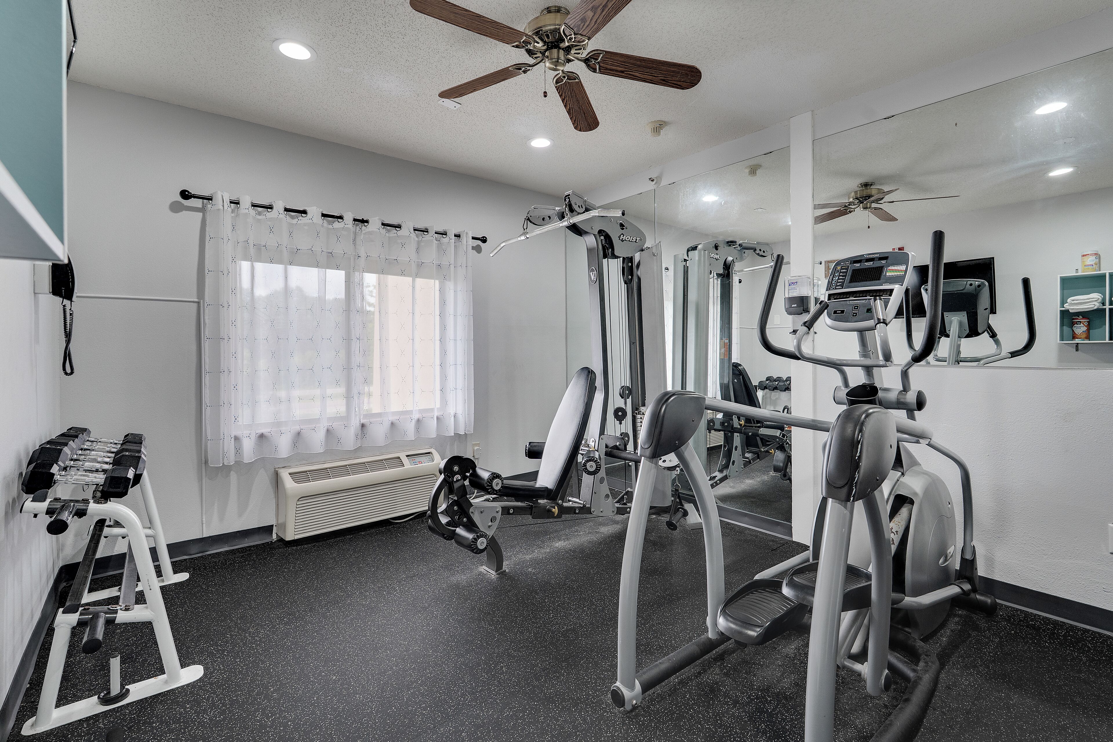 A gym with ceiling fans, exercise equipment, and a window with curtains.