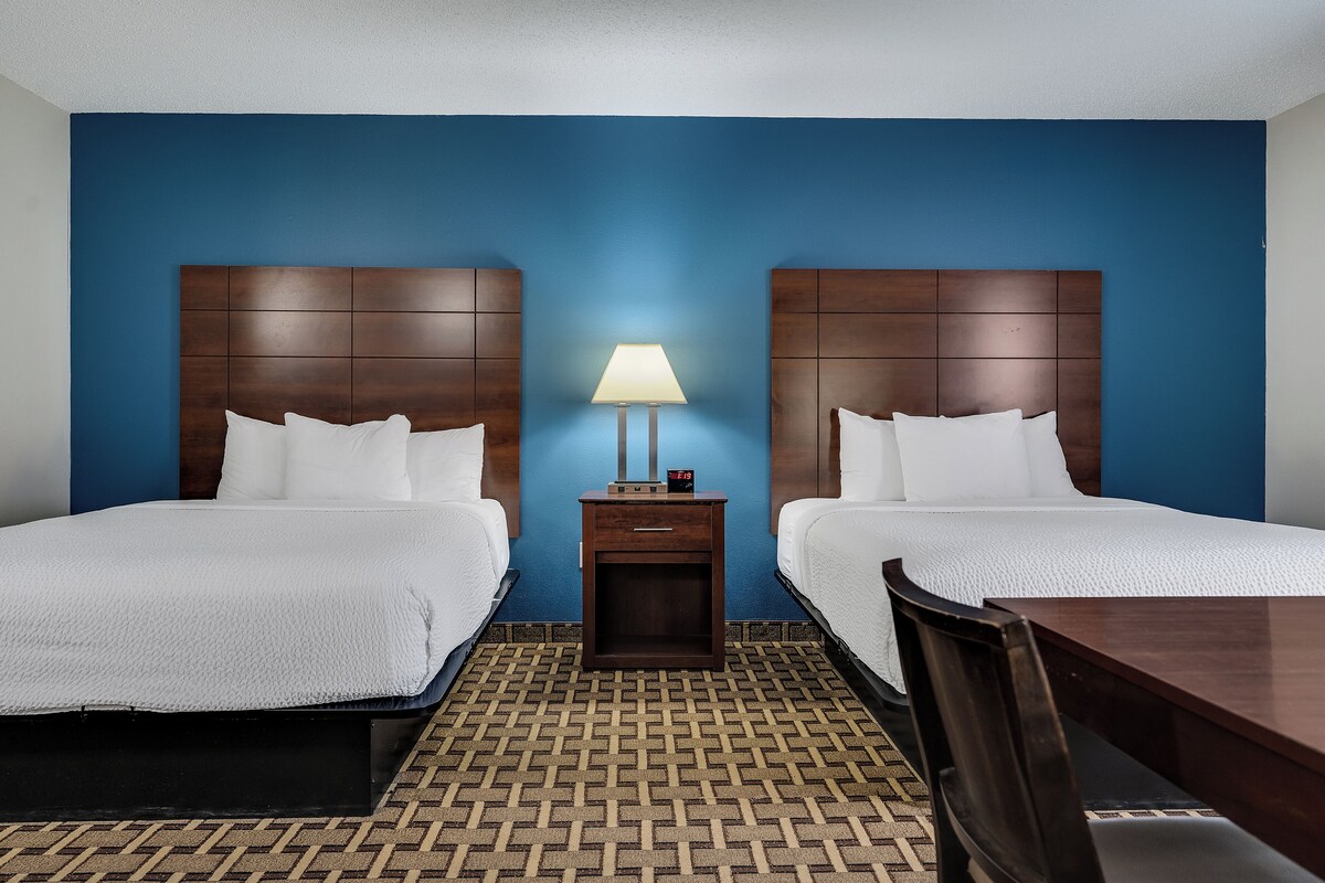 A hotel room with two beds, a nightstand with a lamp, and a wooden table.