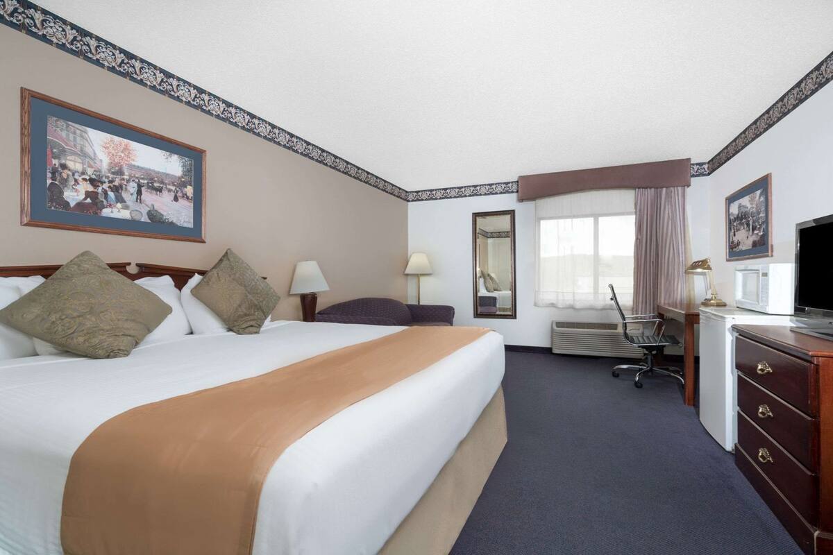 A hotel room with a large bed, a desk, a chair, a television, and a window with curtains.