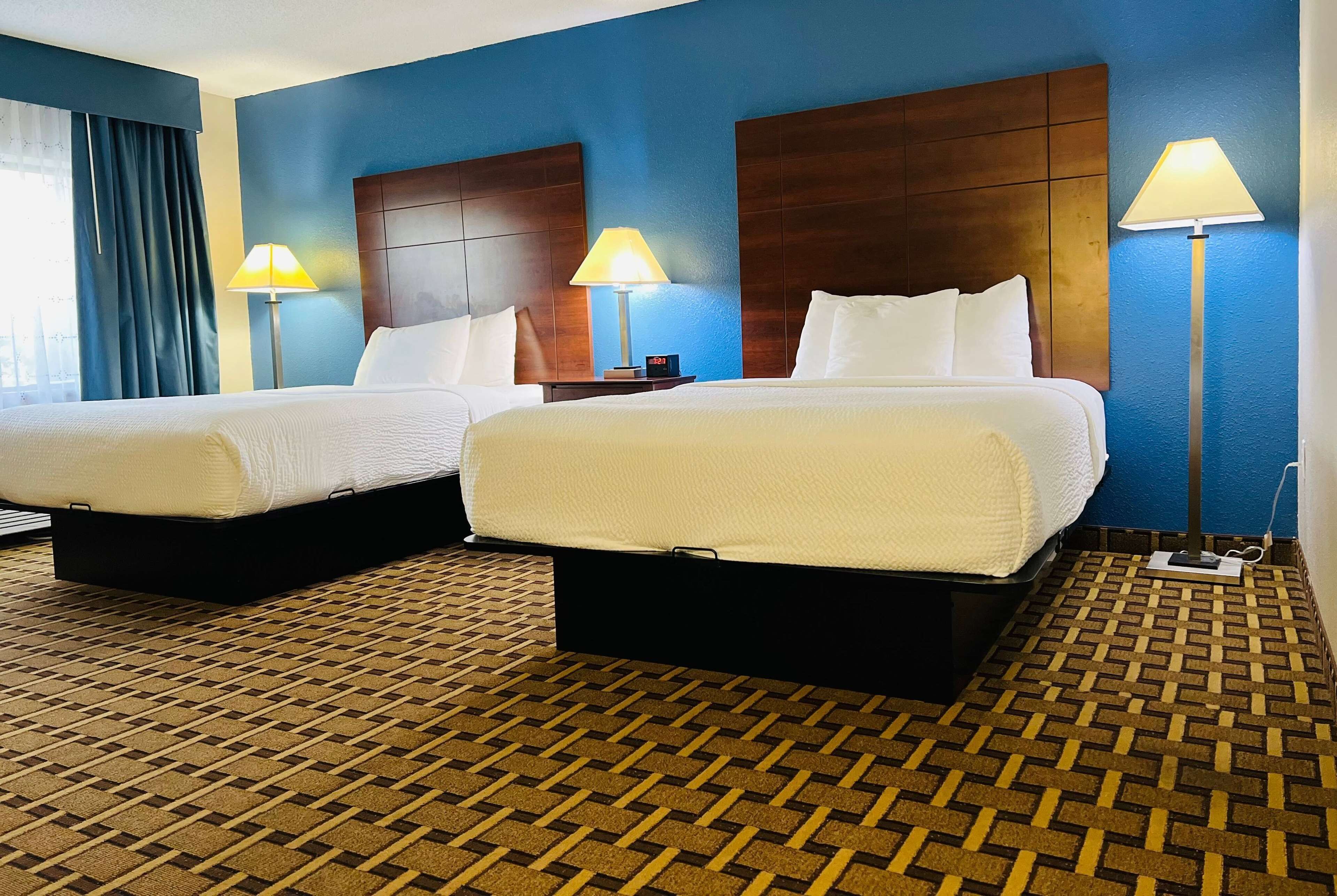 A hotel room with two beds, a patterned carpet, and a blue wall.