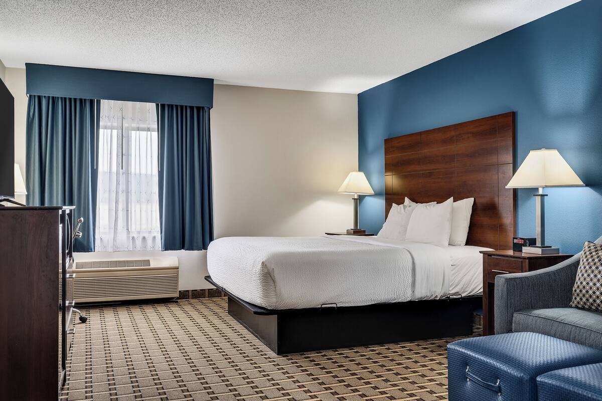 A hotel room with a large bed, two bedside lamps, a desk, and a chair.