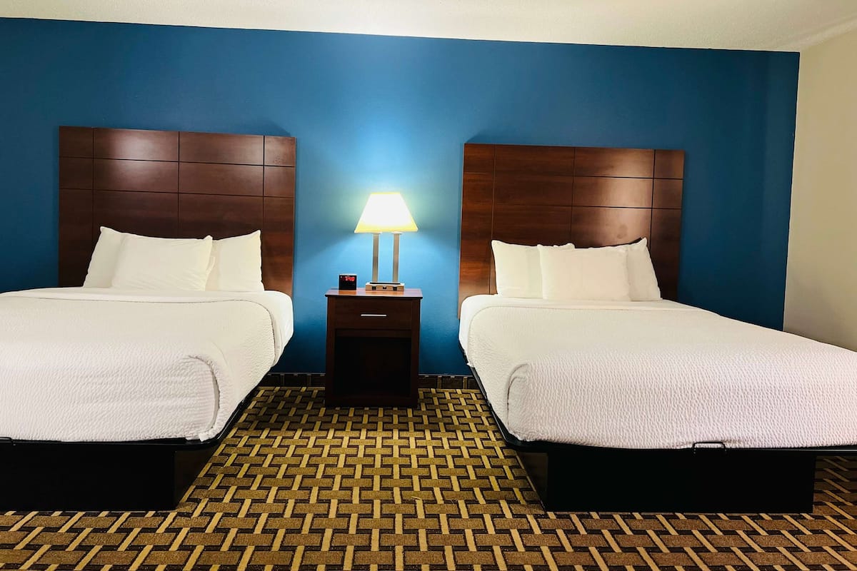 A hotel room with two beds, a nightstand with a lamp, and a patterned floor.
