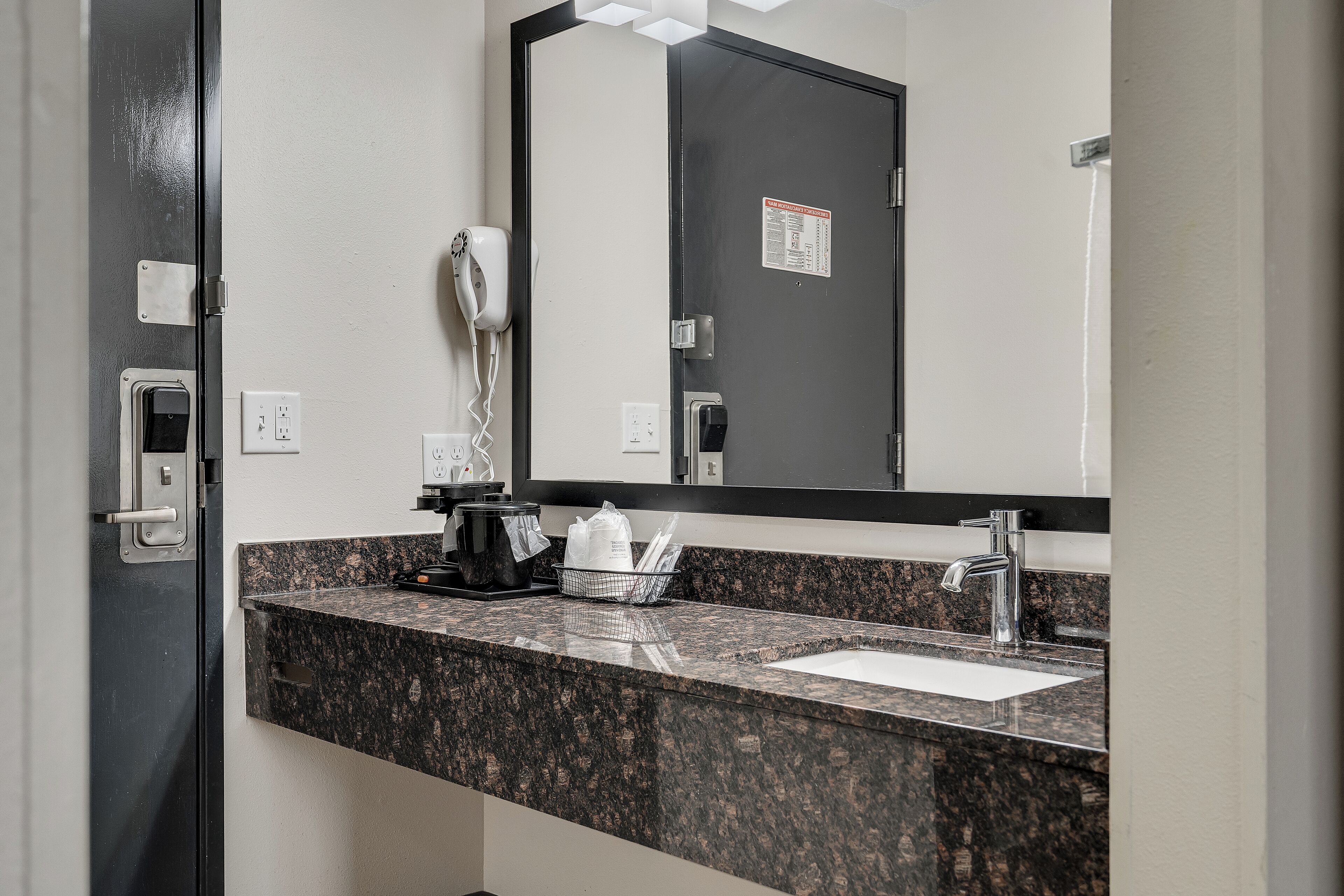 Une salle de bain avec un comptoir en granit, un lavabo, un miroir, un sèche-cheveux et une porte avec une serrure.
