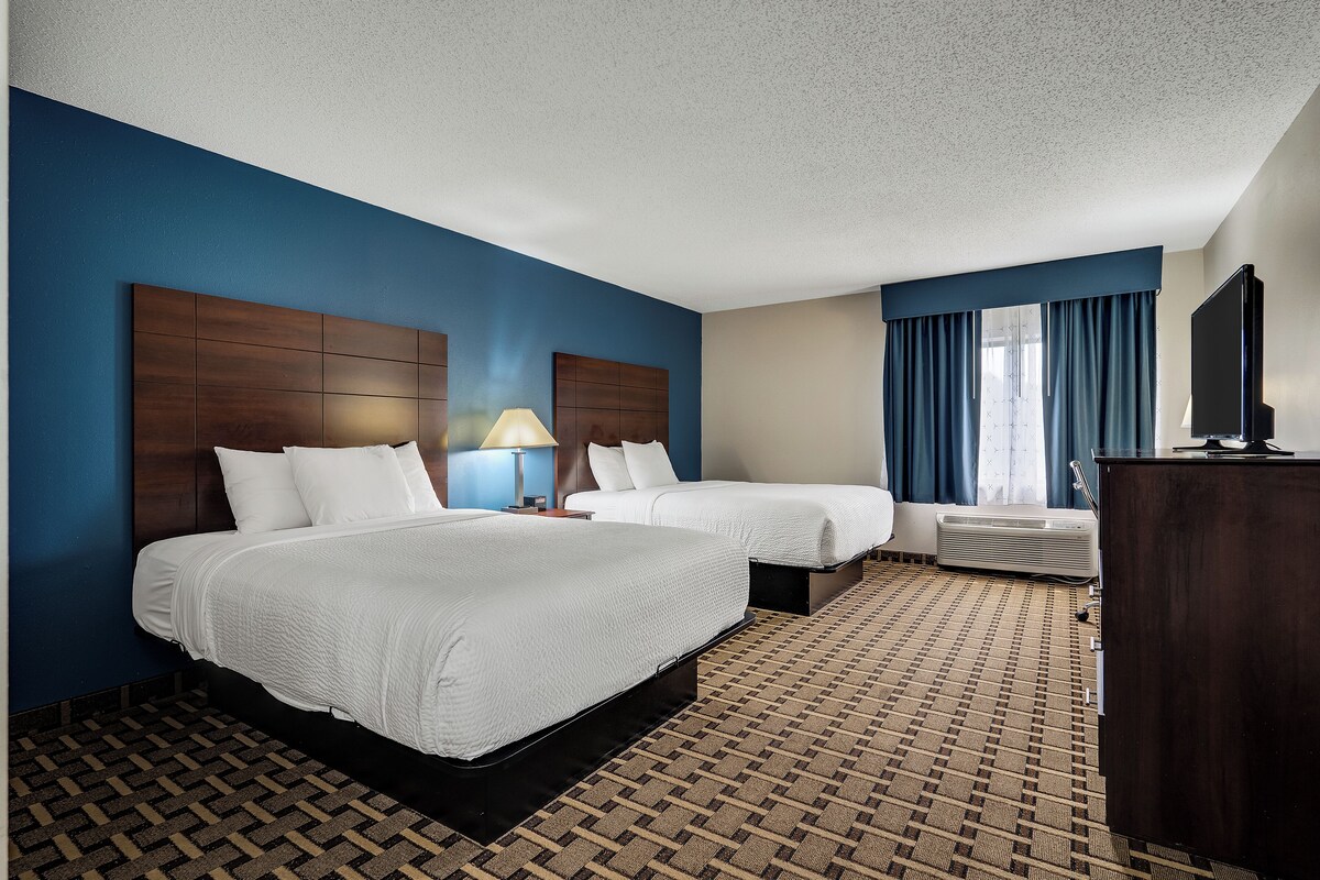 A hotel room with two beds, a TV, a desk, and a window with curtains.
