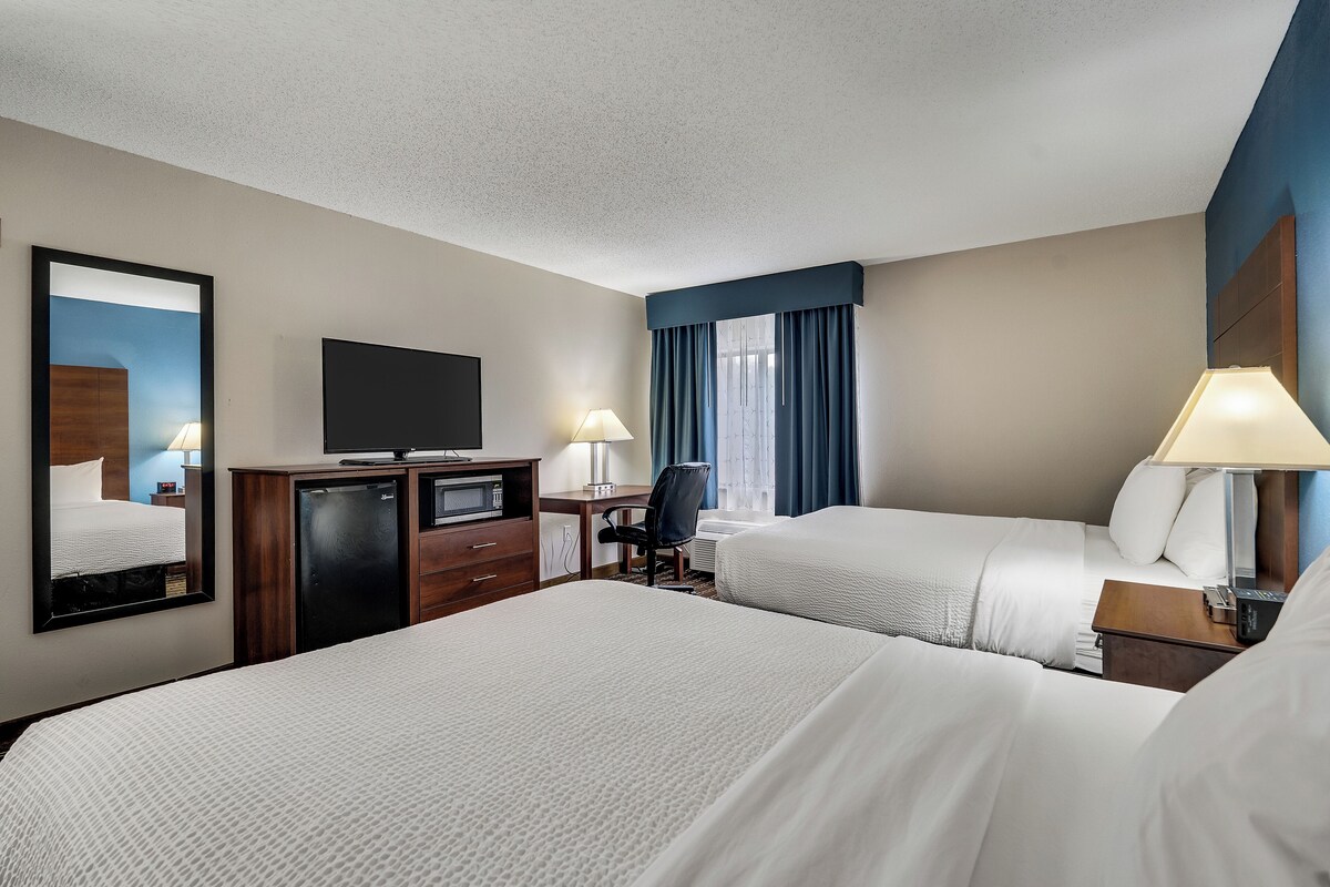 A hotel room with two beds, a desk, a television, and a mirror.