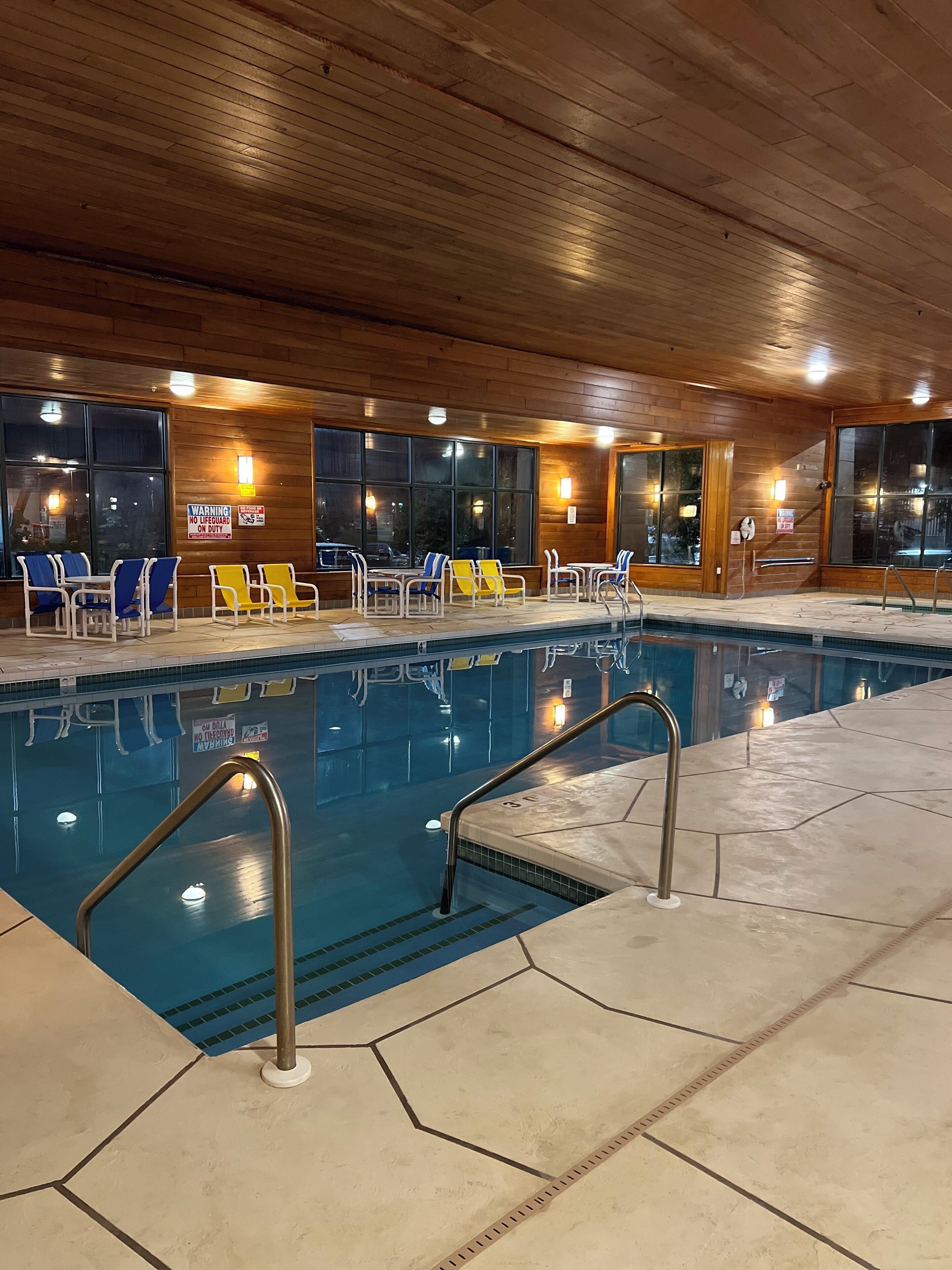 An indoor swimming pool with wooden paneling, multiple lounge chairs, and clear signage.