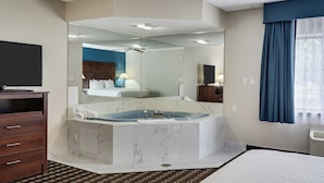 A hotel room with a large bathtub, a wooden dresser, a flat-screen TV, and a large mirror. - Baymont by Wyndham La Crosse/Onalaska (Onalaska)