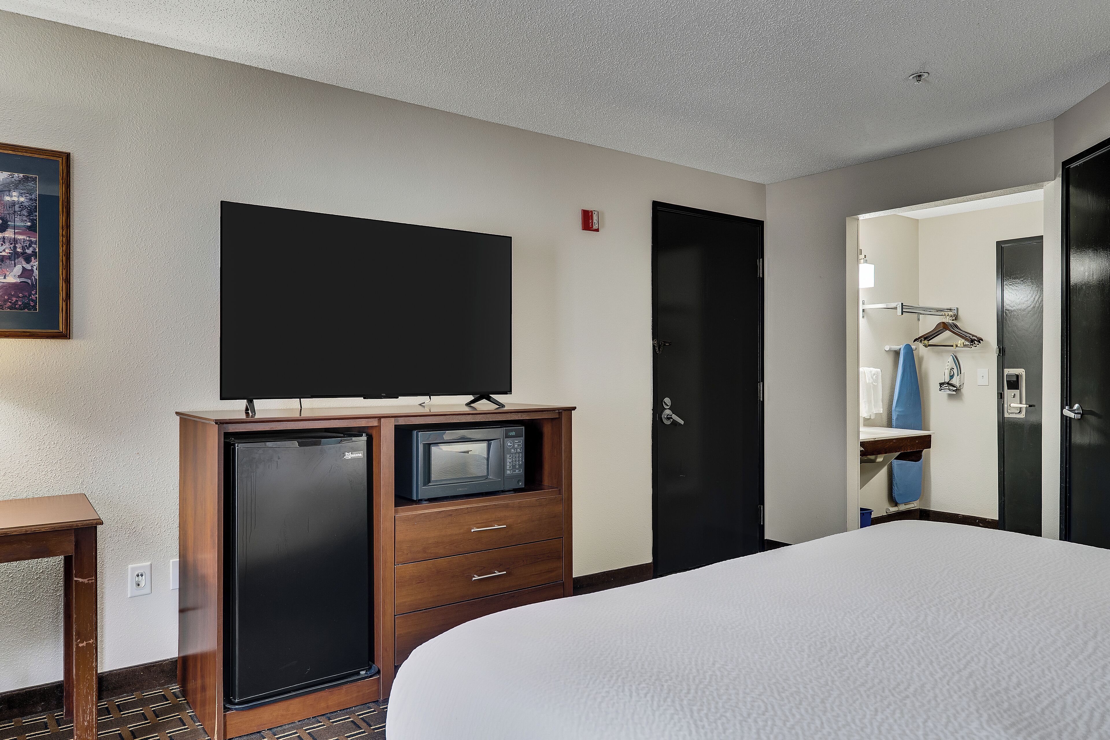 Une chambre d’hôtel avec un lit, un minibar, une télévision, une porte et une salle de bain visible à travers une porte ouverte.