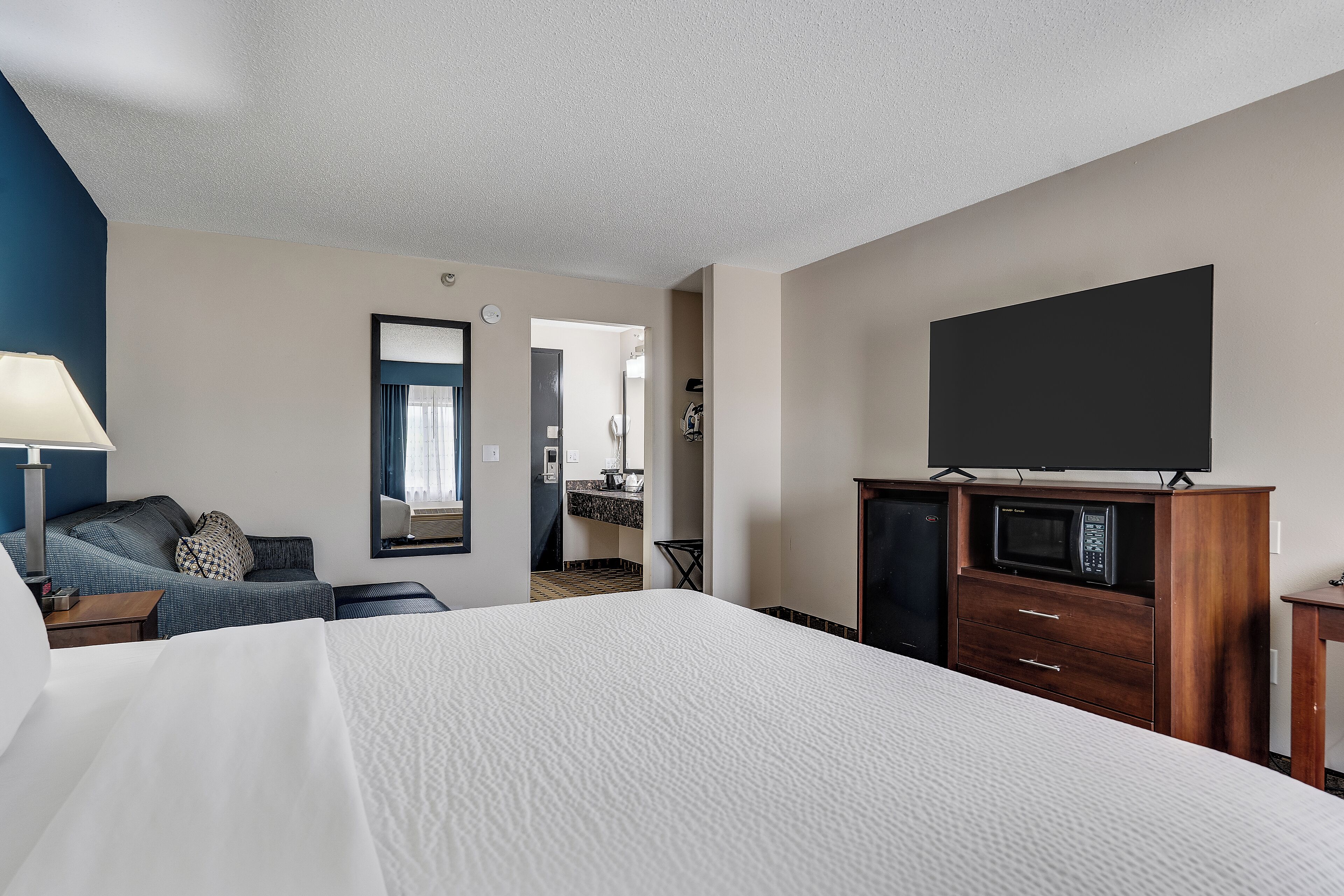 A hotel room with a bed, a TV, a dresser, and a desk.