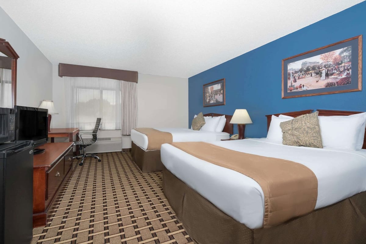 A hotel room with two beds, a desk with a computer, a chair, a TV, and a patterned rug.