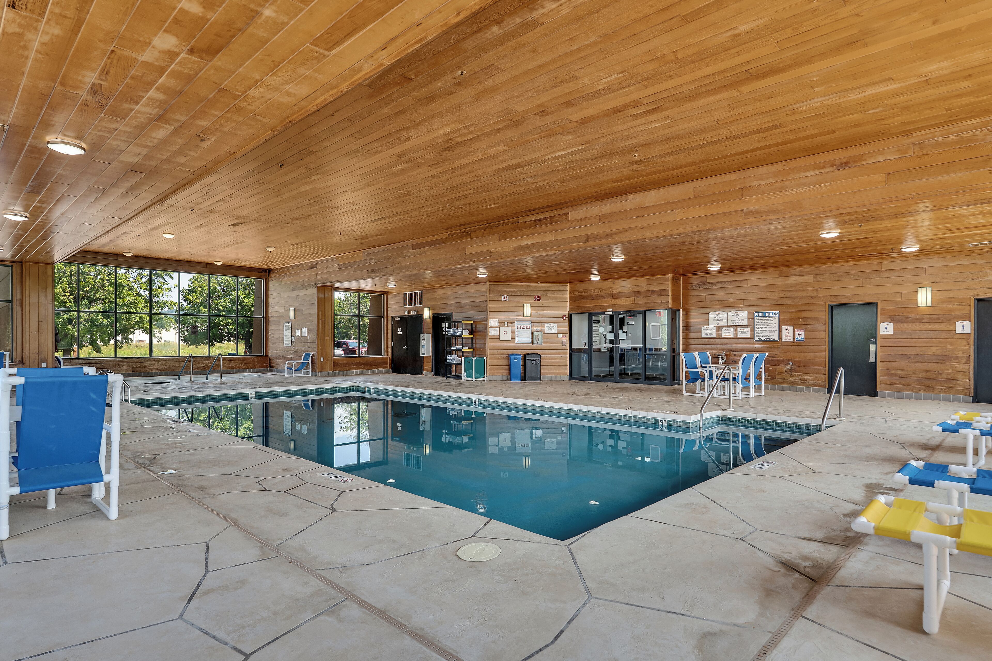 Una piscina interior con paredes de vidrio transparente, techo de madera y suelo de baldosas.