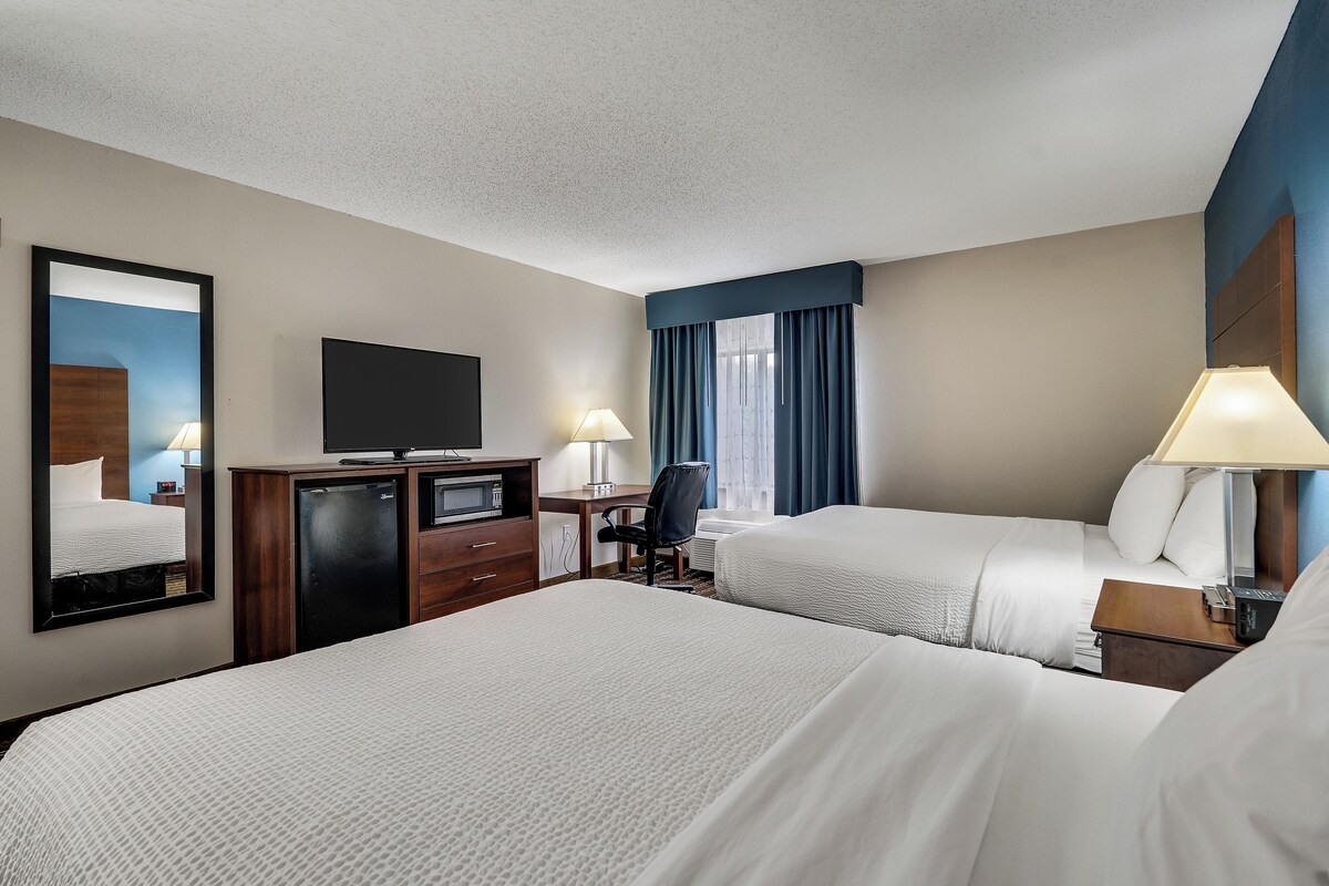 A hotel room with two beds, a desk, a television, and a mirror.