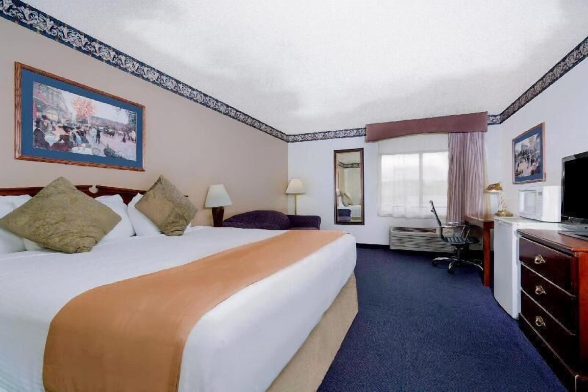 A hotel room with a large bed, a desk, a chair, a television, and a window with curtains.