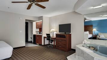A hotel room with a bed, a desk, a chair, a television, a bathroom with a bathtub, and a ceiling fan.
