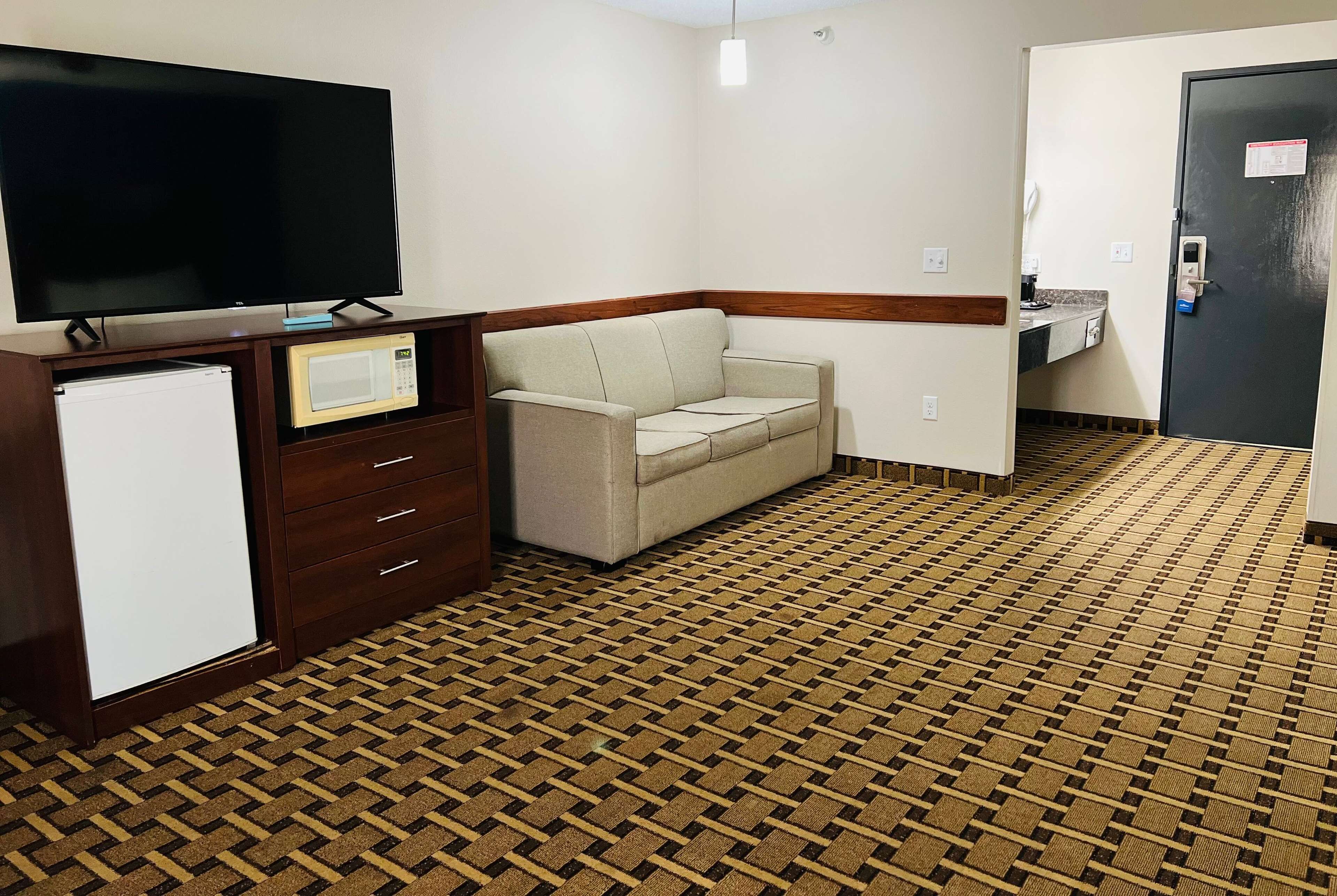 Hotelkamer met flatscreen televisie, magnetron, bank, kleine koelkast en badkamer met wastafel en toilet.