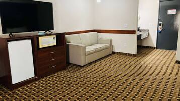A hotel room with a flat-screen TV, a microwave, a sofa, a small refrigerator, and a bathroom with a sink and toilet.