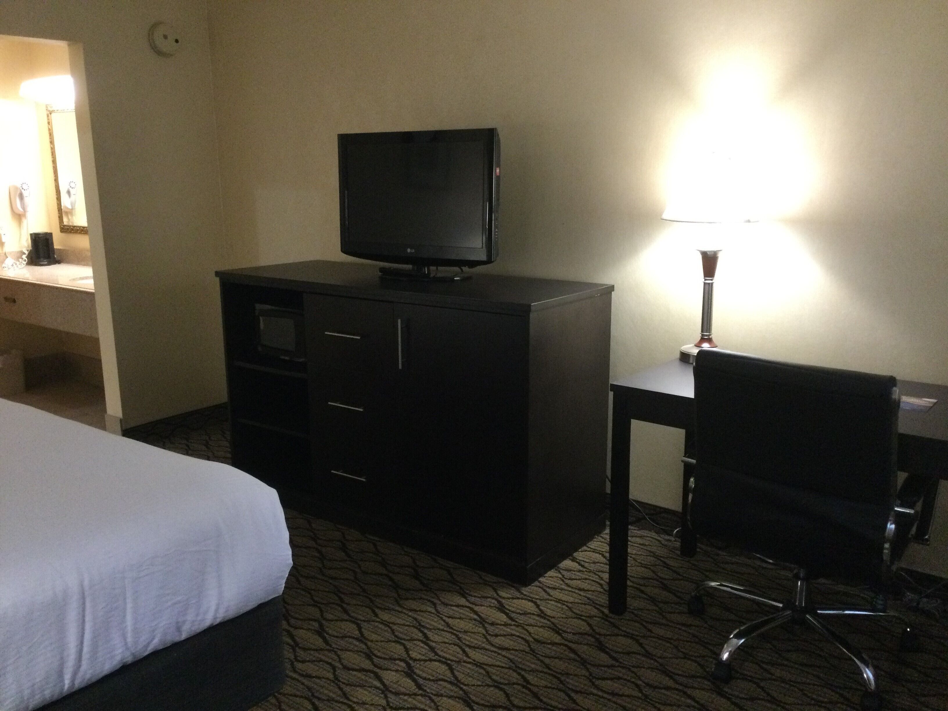 Habitación de hotel con cama, televisor en una cómoda, escritorio con silla y lámpara.