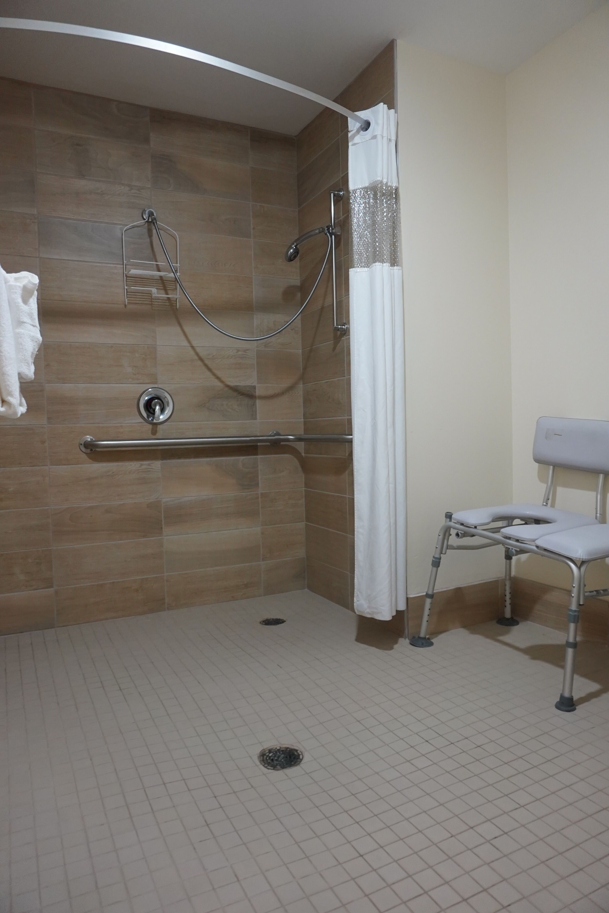 A bathroom with a shower, grab bars, a wheelchair-accessible bench, and a tiled floor.