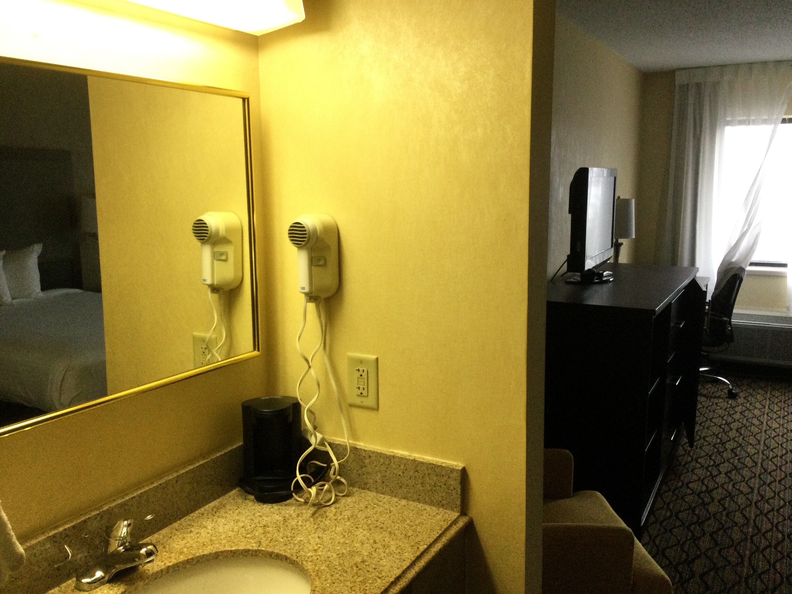 A hotel room with a bathroom, a desk, a chair, and a bed.