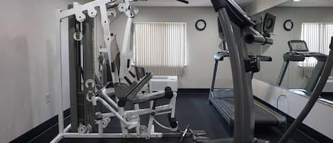 A gym with a treadmill, weight machines, and a mirrored wall.