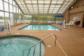 An indoor swimming pool with clear glass walls, lounge chairs, and a covered roof. - Baymont by Wyndham Bridgeport/Frankenmuth (Bridgeport)