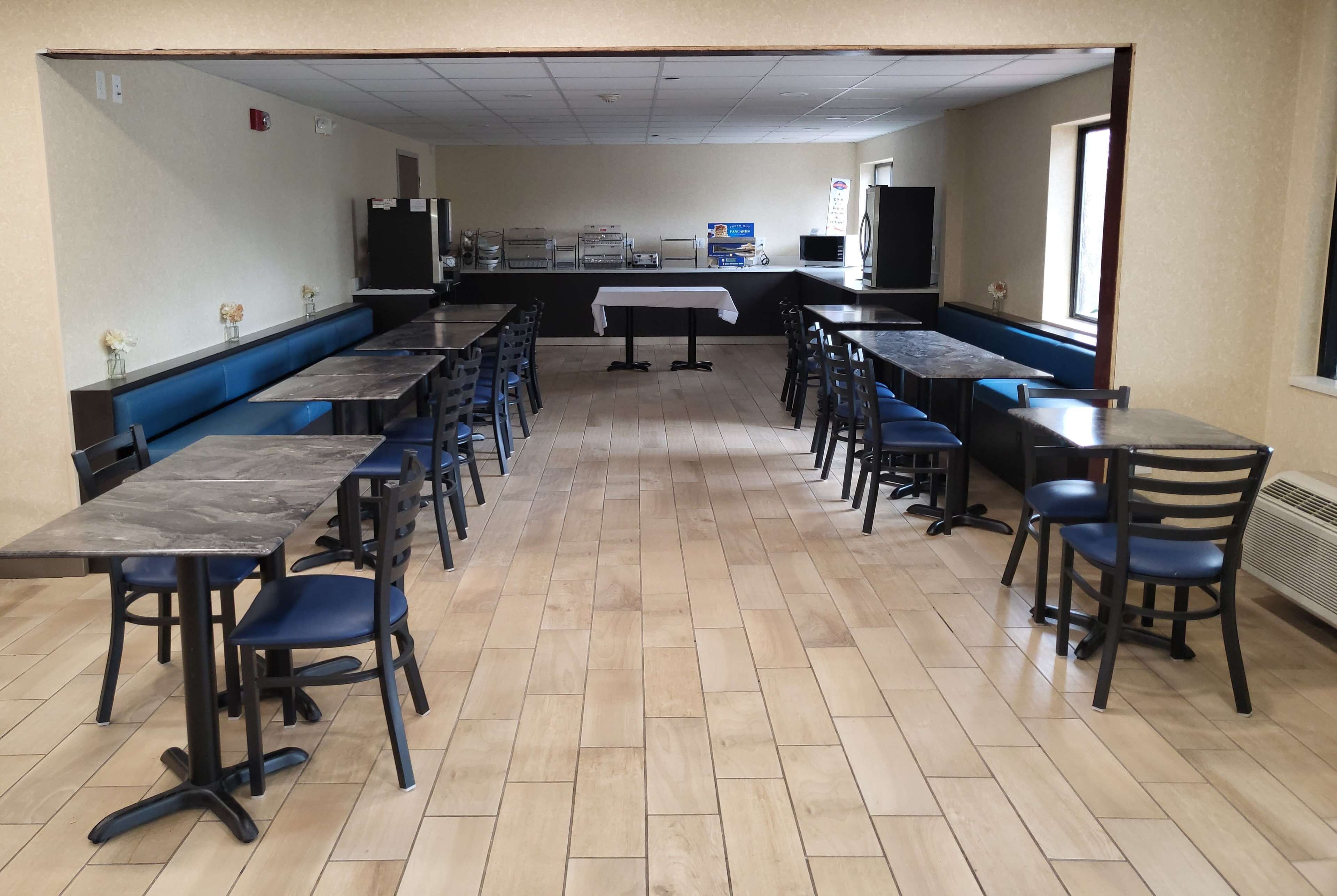 A cafeteria with long tables and benches, a kitchen area, and a window with natural light.