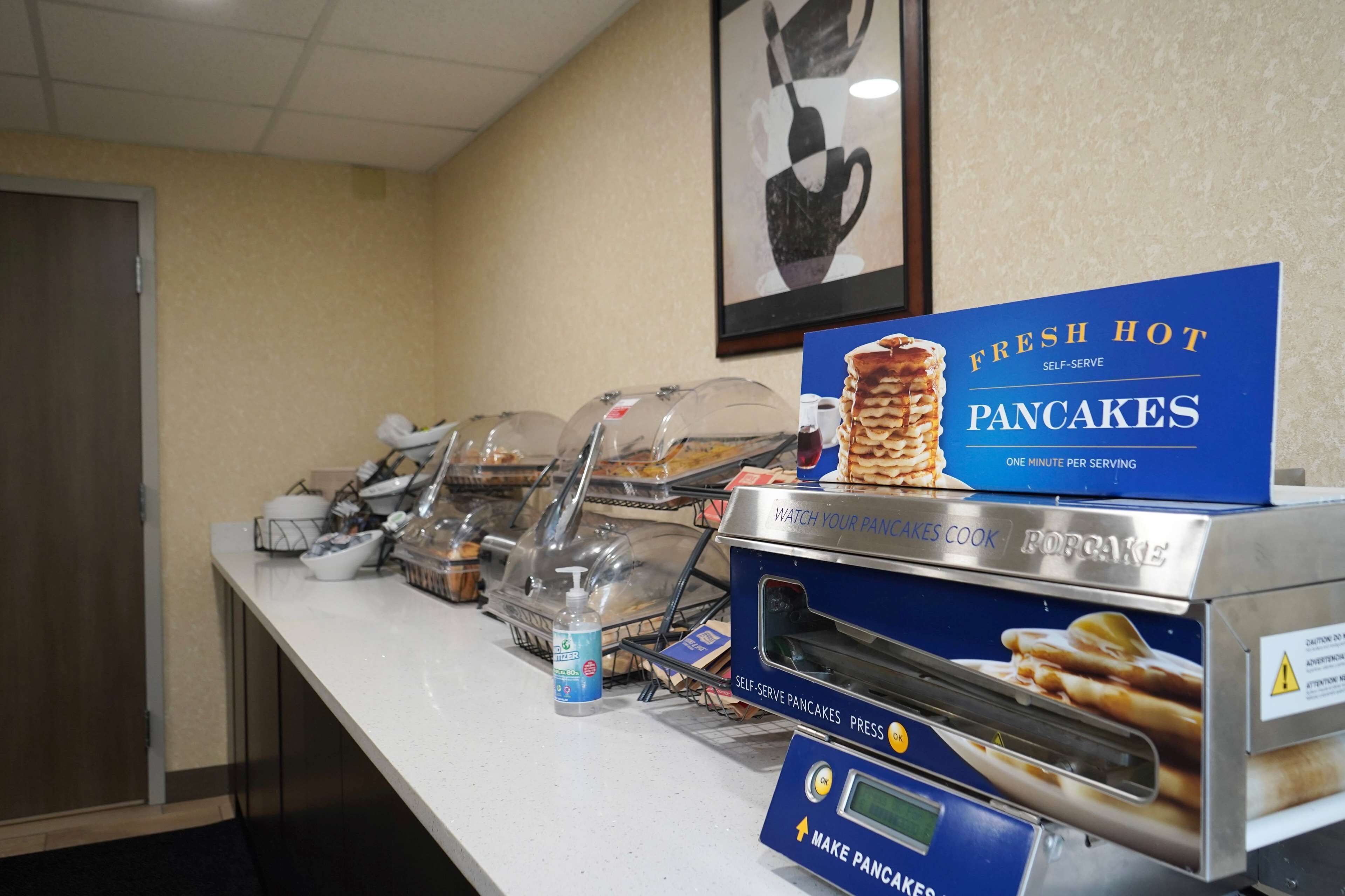 A self-serve pancake station with a sign indicating fresh hot pancakes, a popcorn maker, and a water dispenser.