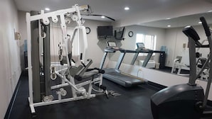 Un gimnasio con equipo de ejercicio, cinta de correr y un espejo grande.