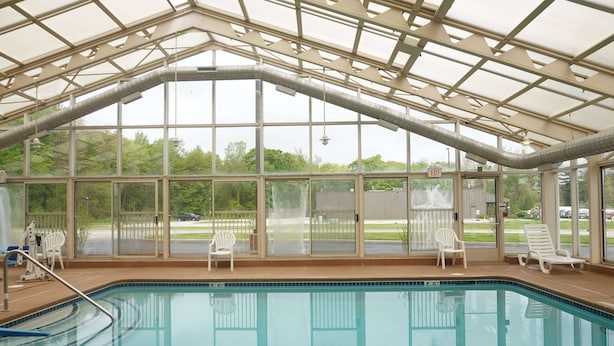 Una piscina con paredes de vidrio transparente, sillas reclinables blancas y una estructura de techo cubierta.