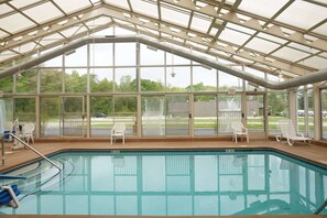 A swimming pool with clear glass walls, white lounge chairs, and a covered roof structure. - Baymont by Wyndham Bridgeport/Frankenmuth (Bridgeport)