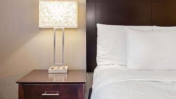 A neatly made bed with white linens, a bedside table with a lamp, and a dark headboard.