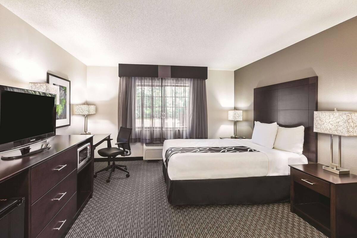 A hotel room with a bed, a desk, a TV, and a chair.