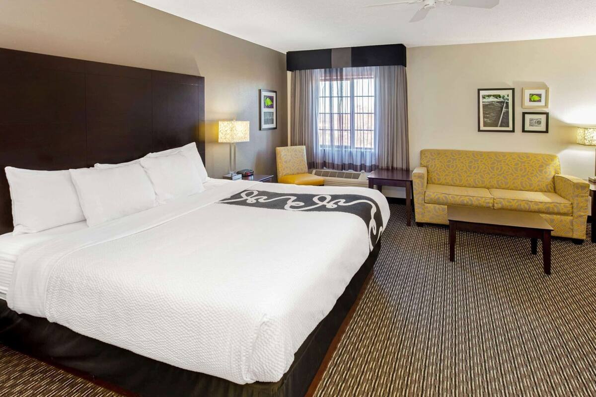 A hotel room with a large bed, a sofa, a chair, a desk, and a window with curtains.