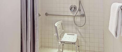 Un área de ducha con barra de apoyo, asiento para ducha y perchero.