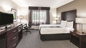 Habitación de hotel con cama, televisor, escritorio, silla y ventana con cortinas.