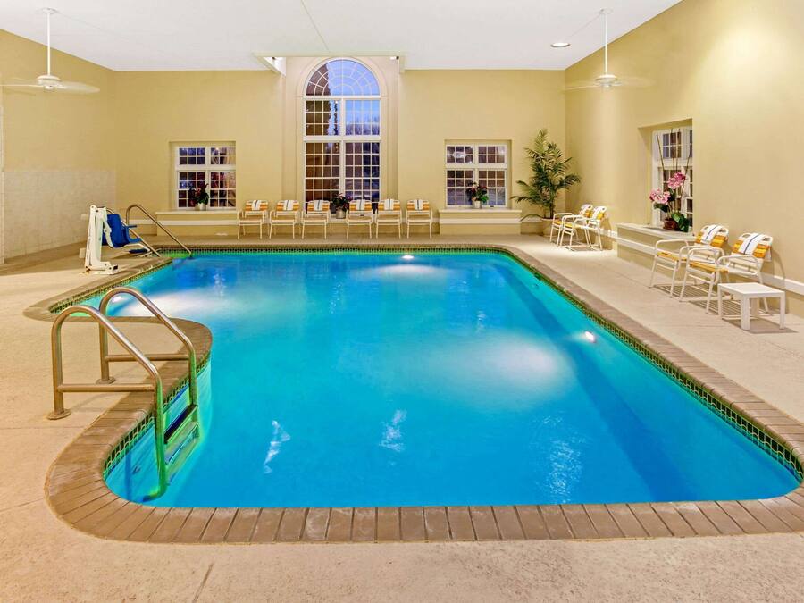 An indoor swimming pool with a clear blue water, surrounded by lounge chairs and a sunbed.
