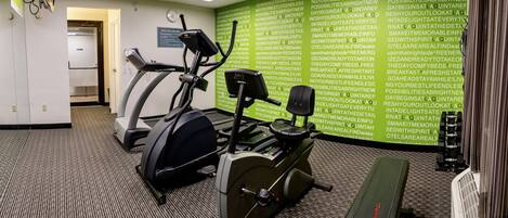 A fitness center with treadmills and an elliptical machine, a clock, and a motivational green wall.