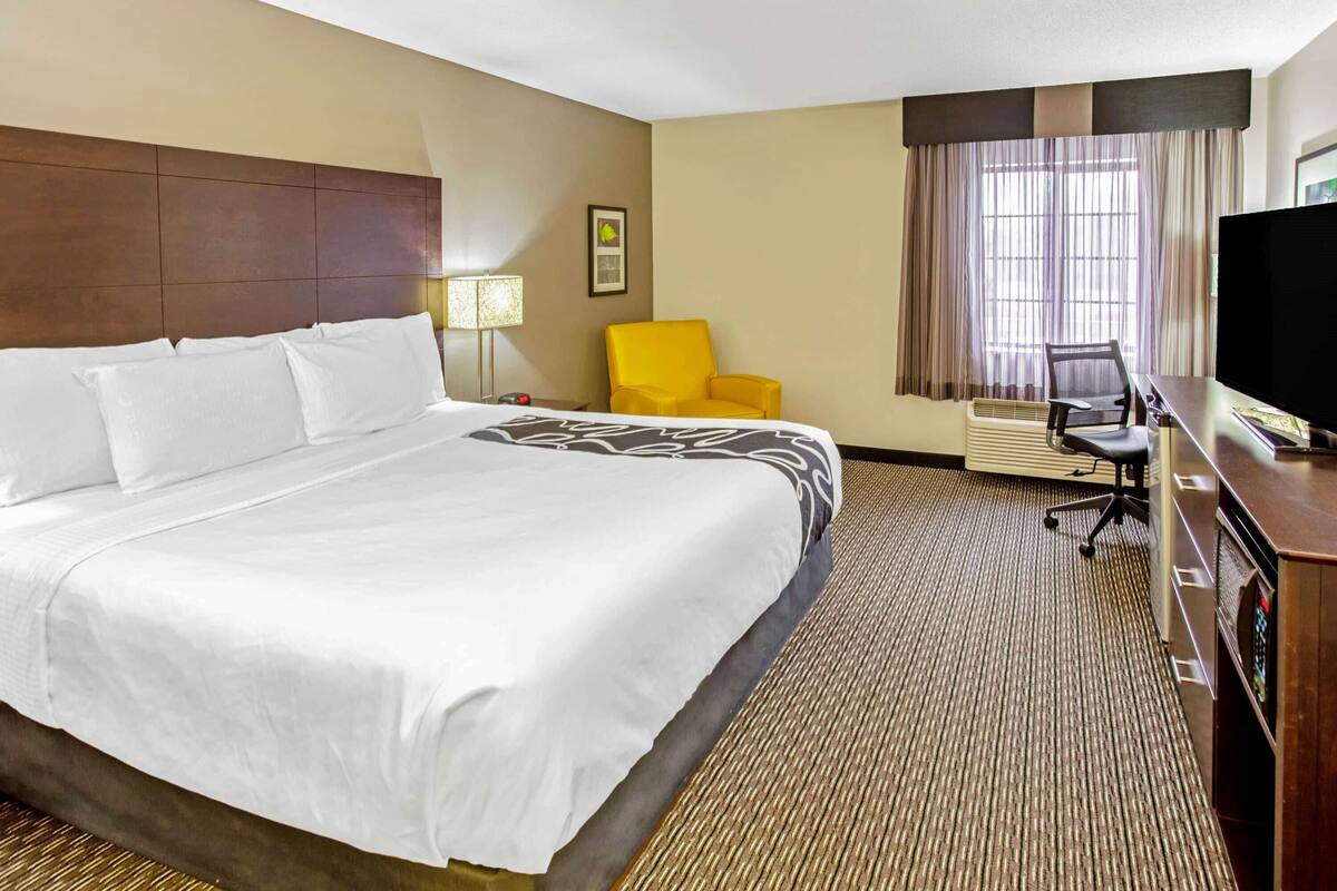 A hotel room with a large bed, a desk with a computer, a chair, a television, and a window with curtains.