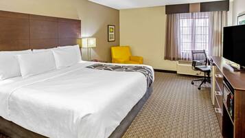 A hotel room with a large bed, a desk with a computer, a chair, a television, and a window with curtains.
