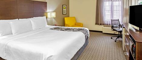 A hotel room with a large bed, a desk with a computer, a chair, a television, and a window with curtains.