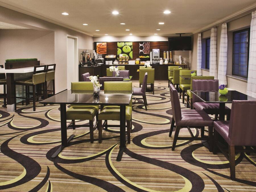 Une salle à manger d’hôtel avec plusieurs tables et chaises, une cuisine en arrière-plan et un tapis à motifs.