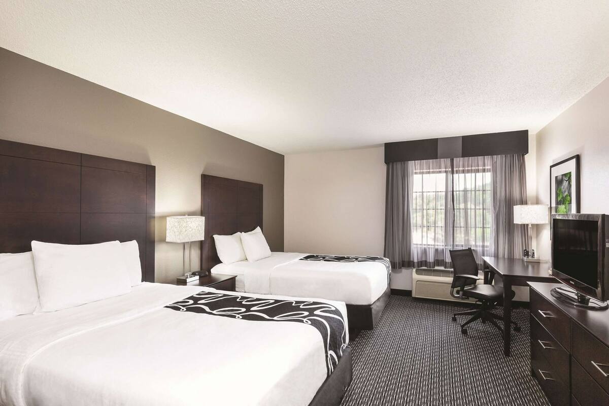 A hotel room with two beds, a desk, a chair, a TV, and a window with curtains.