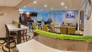 Un vestíbulo de hotel con zona de comedor, mostrador de recepción y un reloj en la pared.
