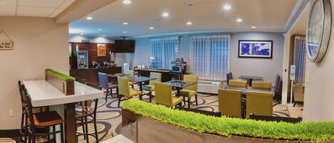 A hotel lobby with a dining area, a reception desk, and a clock on the wall.